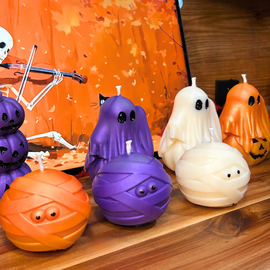 Halloween-themed candles shaped like ghosts, pumpkins, and mummies on a wooden surface with an orange background.
