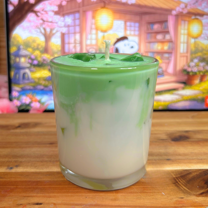 Green and white layered candle in a glass container on a wooden surface with a colorful background.