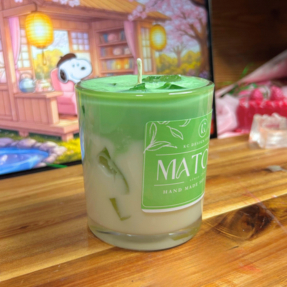 Green candle labeled 'Matcha' on a wooden surface with a blurred background