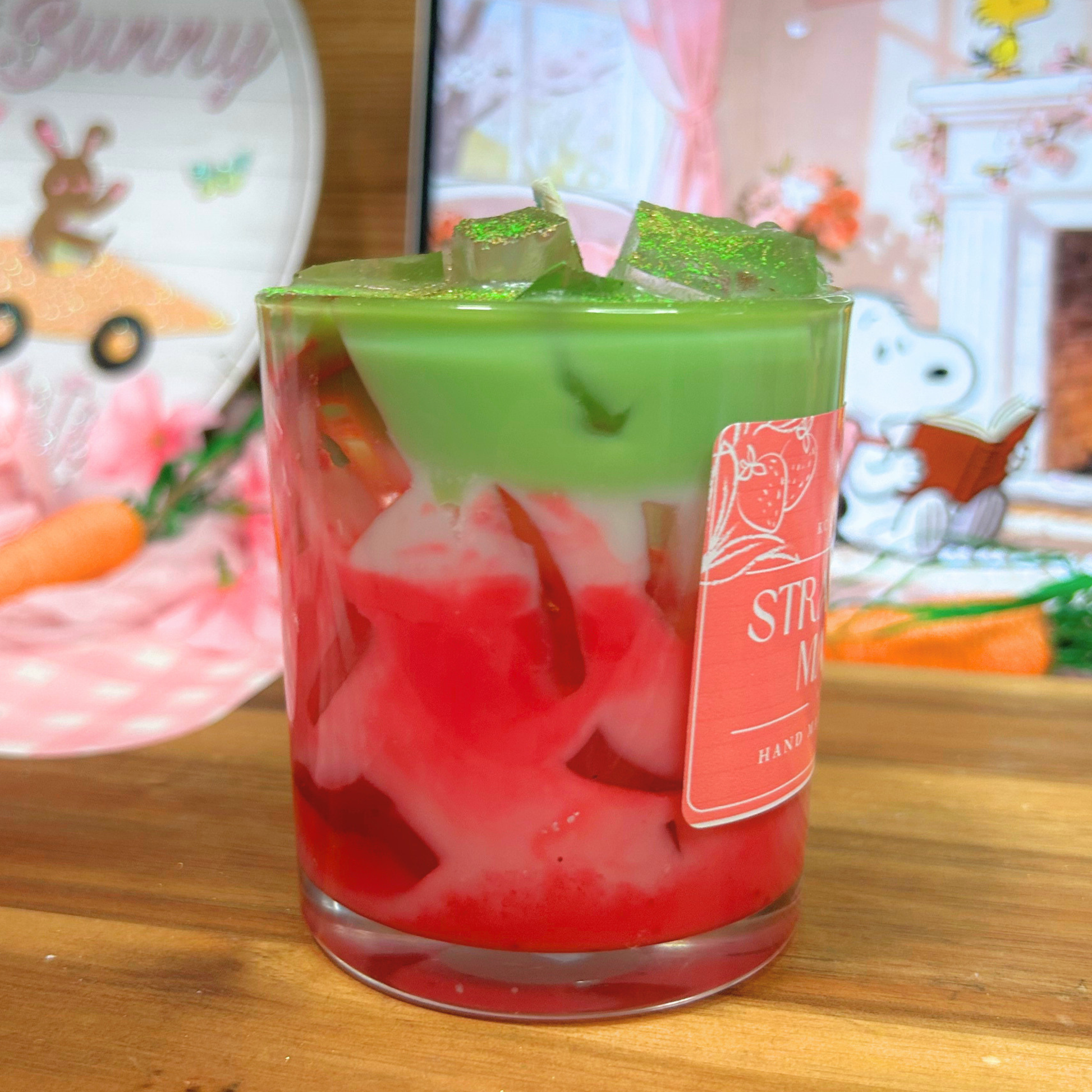 Glass of strawberry matcha candle on a wooden surface, with Easter-themed decorations in the background.