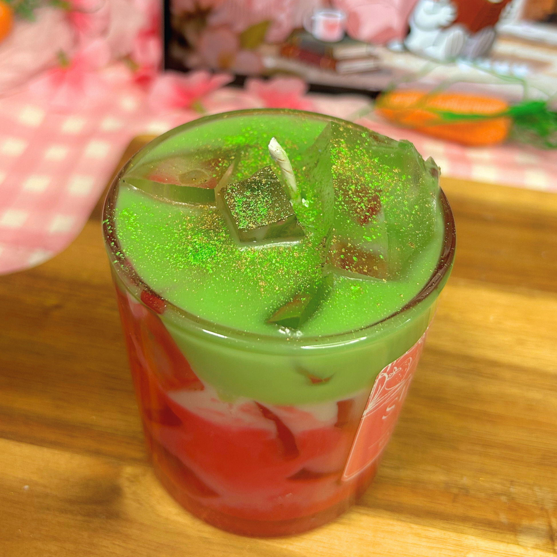 Strawberry Matcha candle with ice on top in a transparent glass on a wooden surface.