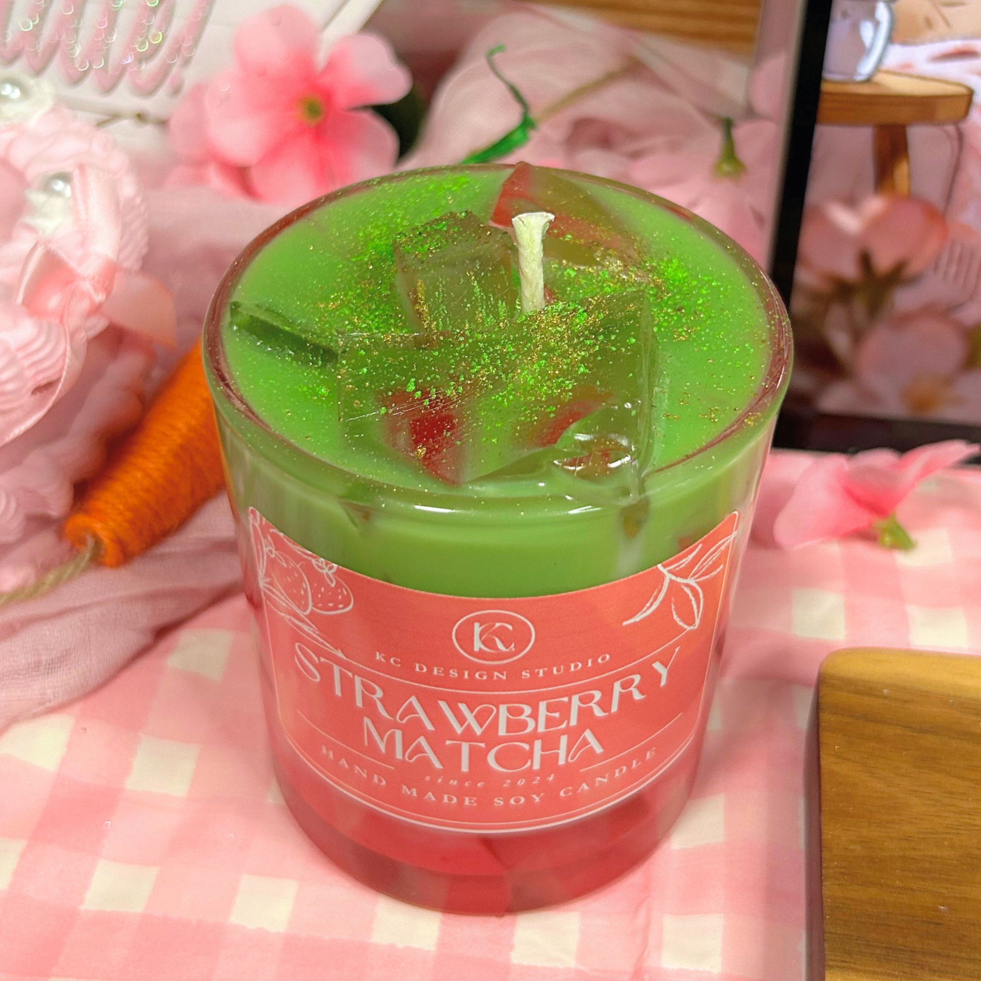 Green 'Strawberry Matcha' candle with decorative elements on a pink checkered background