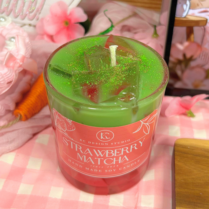 Green 'Strawberry Matcha' candle with decorative elements on a pink checkered background