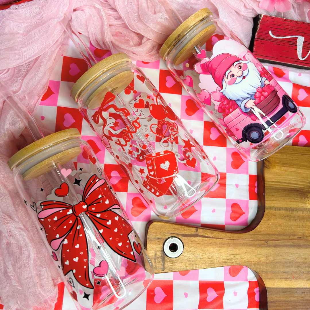 Three clear tumblers with decorative valentine designs on a pink checkered tablecloth.