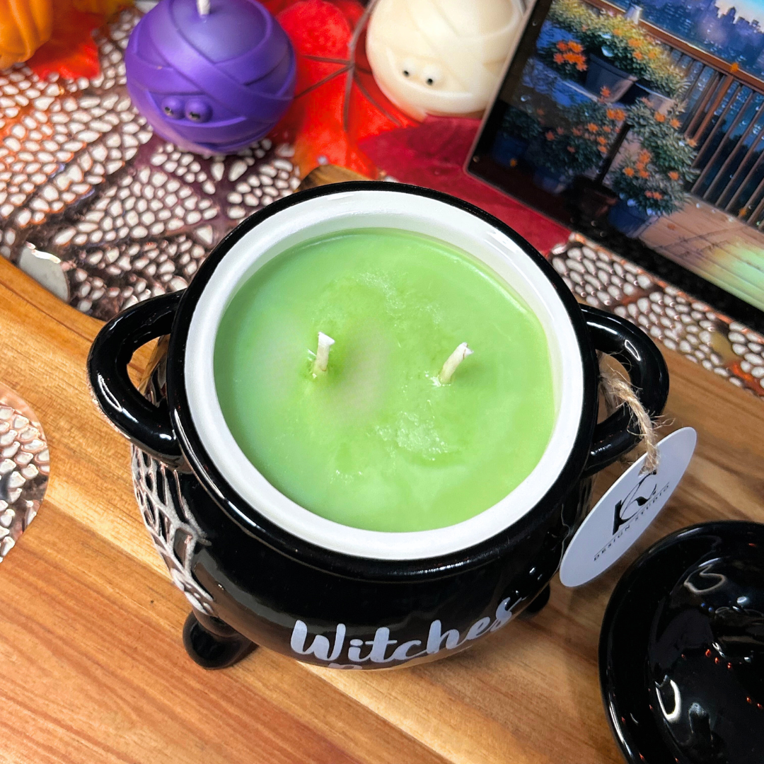 Green witches brew candle in a black cauldron on a wooden surface with Halloween decorations.
