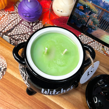Green witches brew candle in a black cauldron on a wooden surface with Halloween decorations.