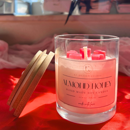Front view of an almond honey and pink grapefruit scented candle, topped with five mini hearts. The lid is placed on the side for a cozy, elegant display.
