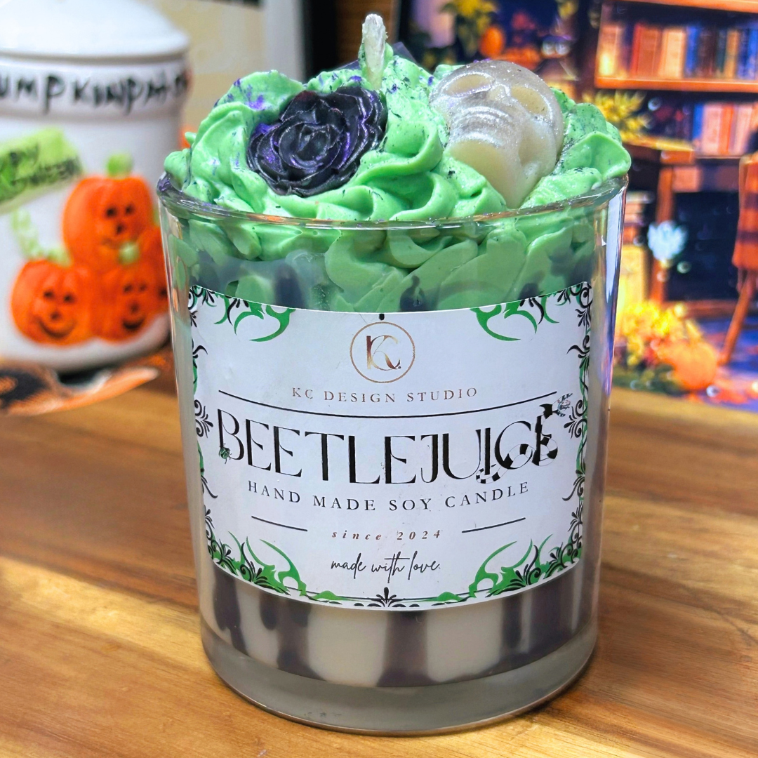 Beetlejuice-inspired 10 oz soy candle with black stripes around the glass, a white wax base, green whipped wax topping, white skull, black grave, and black roses.
