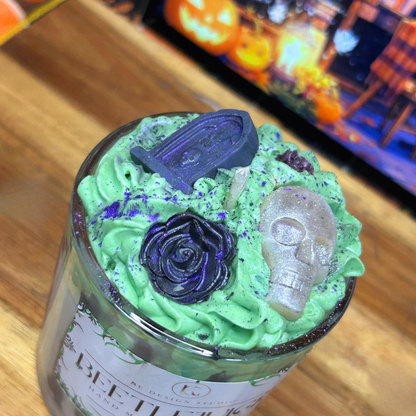 Top view of Beetlejuice-inspired candle featuring green whipped wax, a white skull, black grave, black roses, and purple and black mica details.