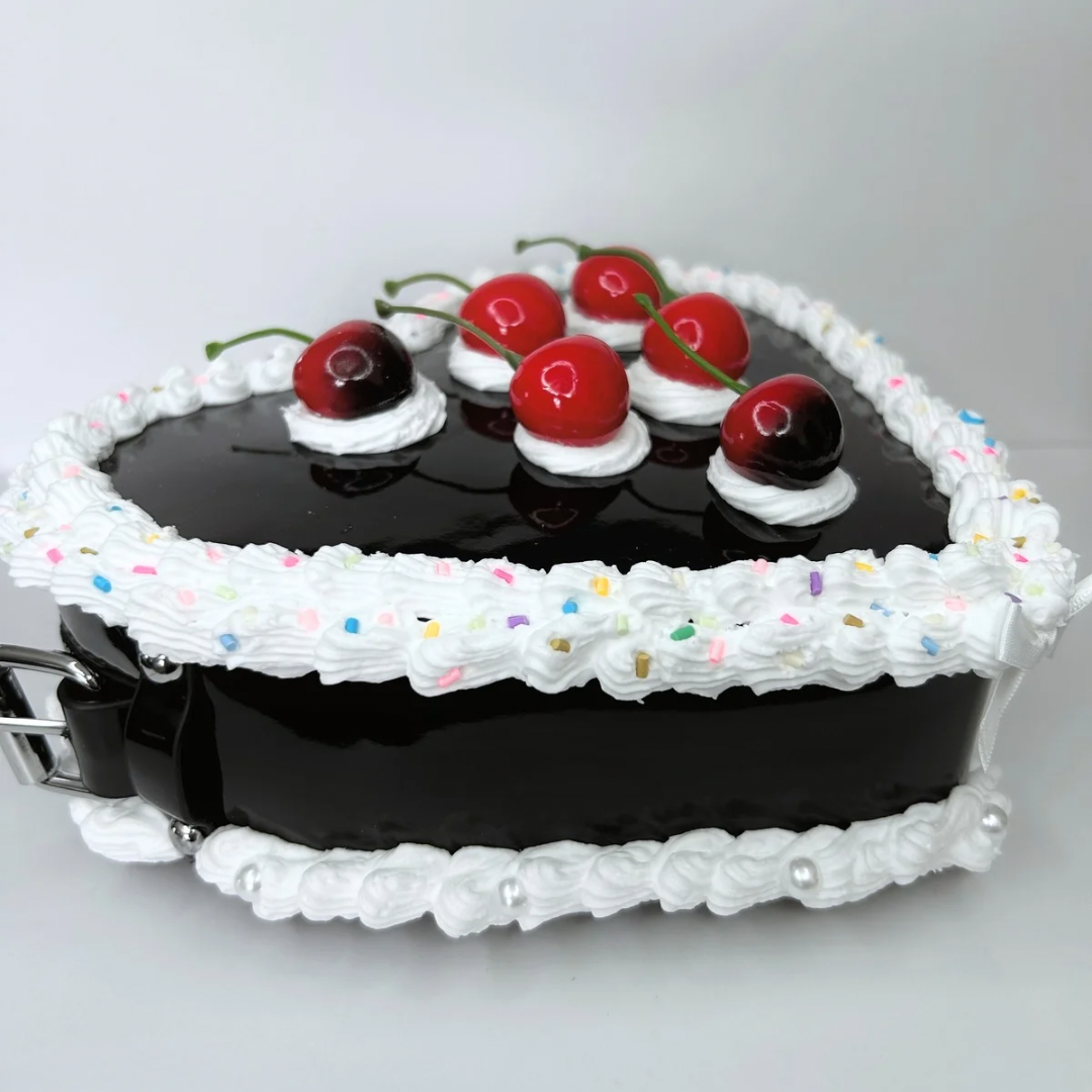 Side view of the black heart-shaped purse showcasing its unique cherry cake design with frosting, sprinkles, and vibrant cherries.