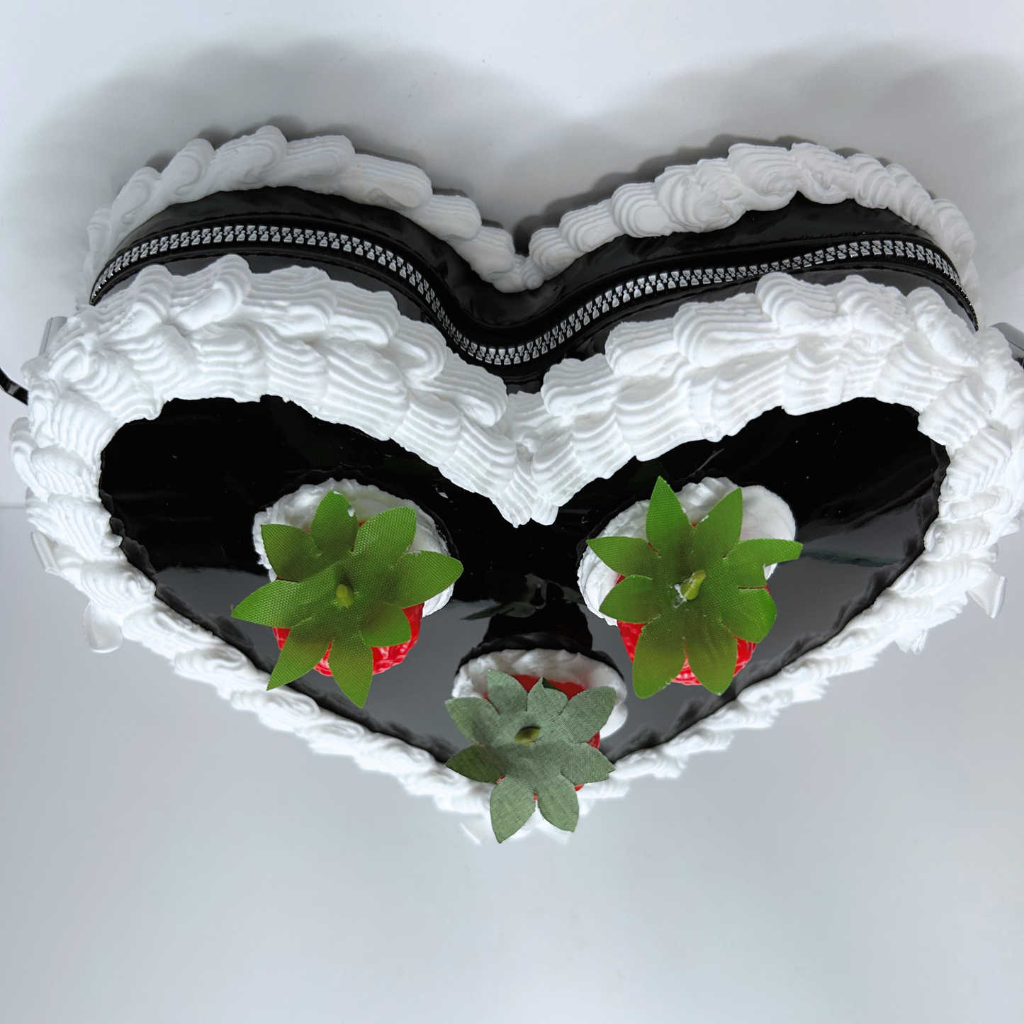 Top view of black heart-shaped strawberry cake purse showcasing zipper and frosting design.