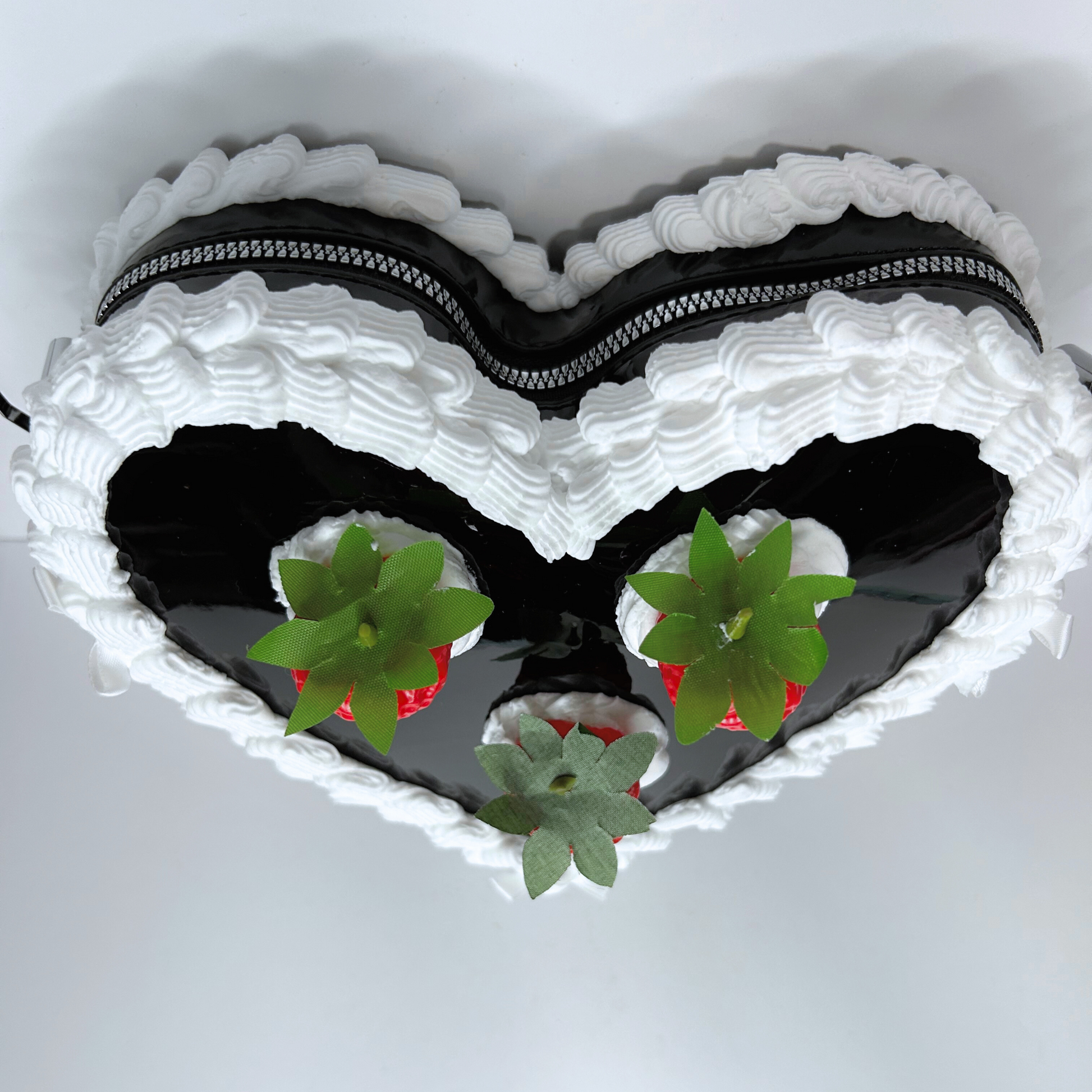 Top view of black heart-shaped strawberry cake purse showcasing zipper and frosting design.