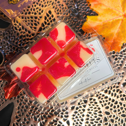 Packaged wax melts with red and white design on a decorative surface with leaves.