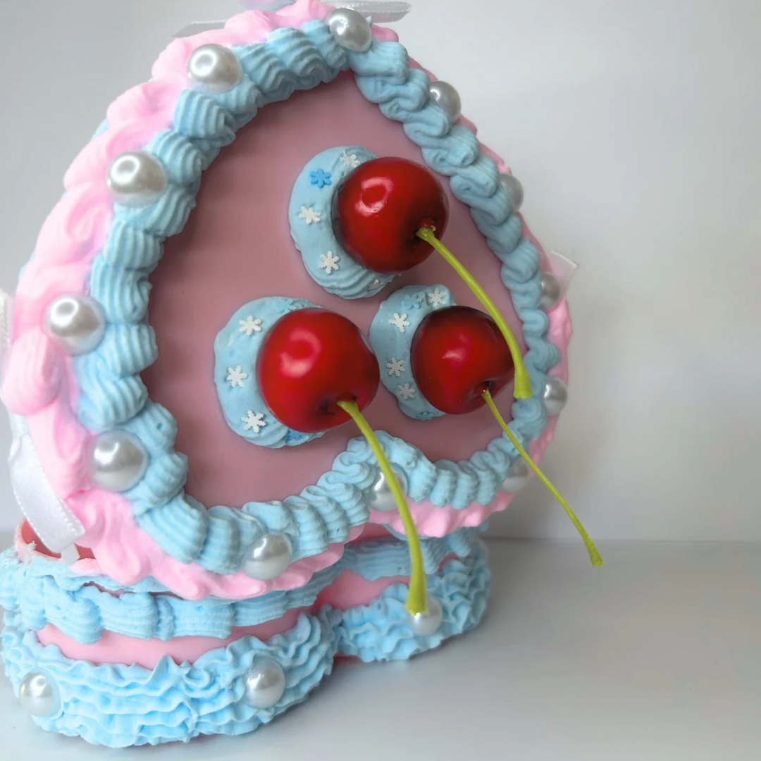 Back open view of the Blue Vintage Heart-Shaped Jewelry Box, featuring its exterior space with red cherries, soft blue cream, and decorative accents of pearls and white bows.