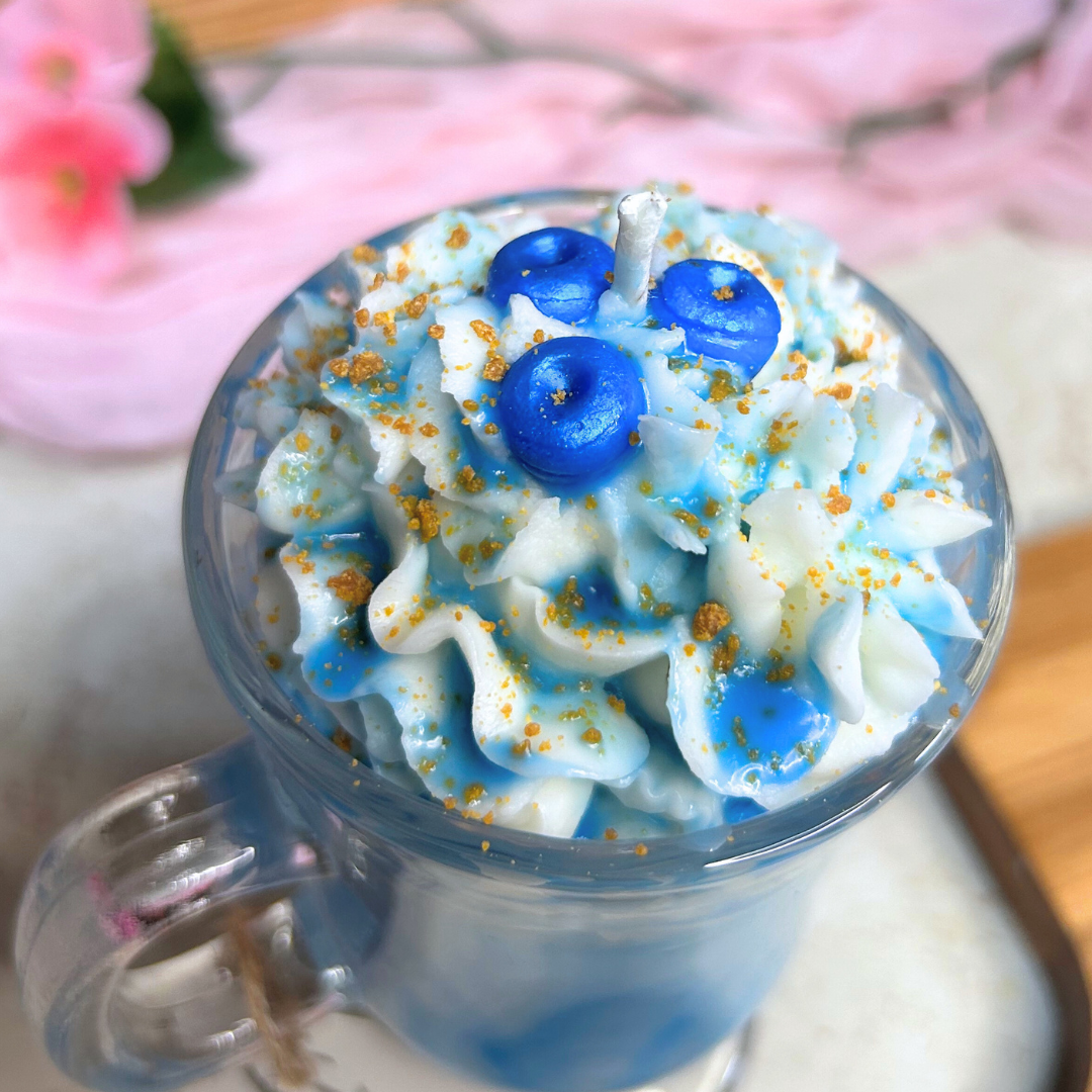 Angled close-up of Blueberry Milkshake Candle highlighting whipped cream, syrup swirls, caramel crumbs, and blueberries on a pink background