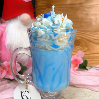 Side view of Blueberry Milkshake Candle showing light blue wax base, blueberry syrup drizzle, and whipped cream topping on a pink flower background