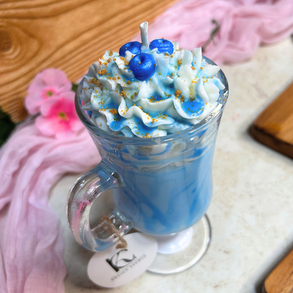 Top view of Blueberry Milkshake Candle in a clear Irish coffee mug with whipped cream, blueberries, and caramel crumbs on a pink flower background