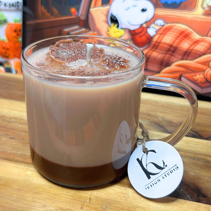 A clear glass mug candle filled with a layered design, topped with a brown powder on an autumn-themed background. 