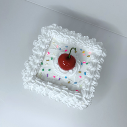 Top view of square wooden storage box with white frosting, rainbow sprinkles, and cherry topper.