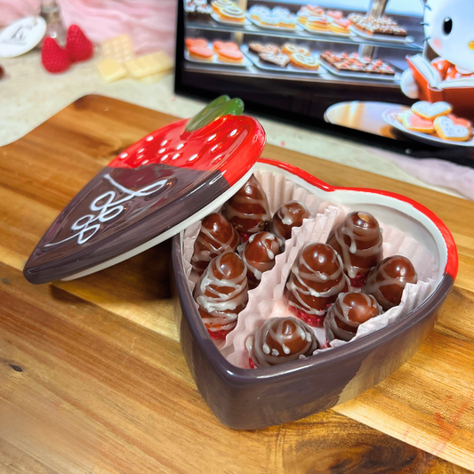 Open box of chocolate covered strawberry wax melts in a strawberry trinket box on a wooden surface with a pink Valentine’s background