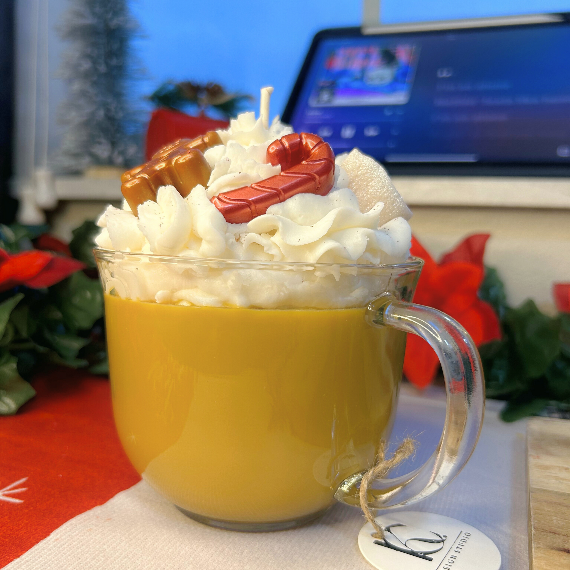 Low angle view of the Christmas Hot Chocolate candle in a glass mug with holiday-themed toppings and brown creamy base layer.