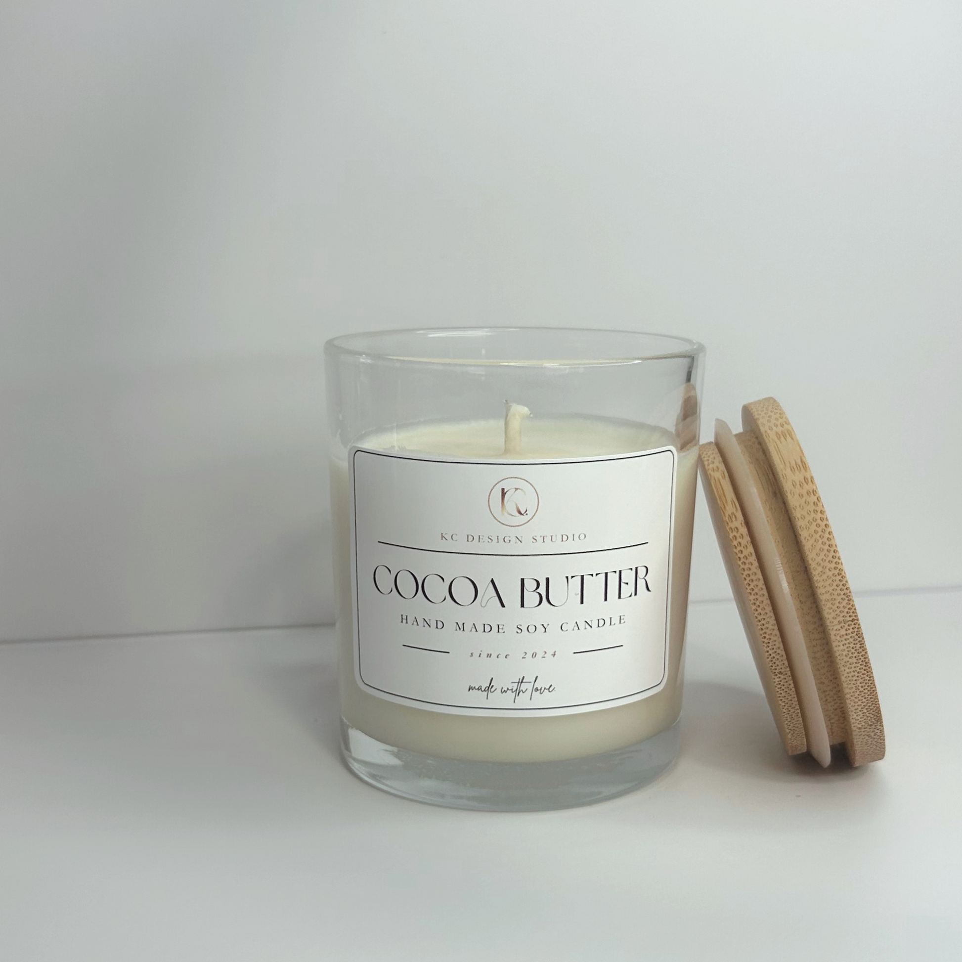 Front view of the 10oz Cocoa Butter candle with the lid resting on the side, highlighting its stylish vessel and inviting aroma.