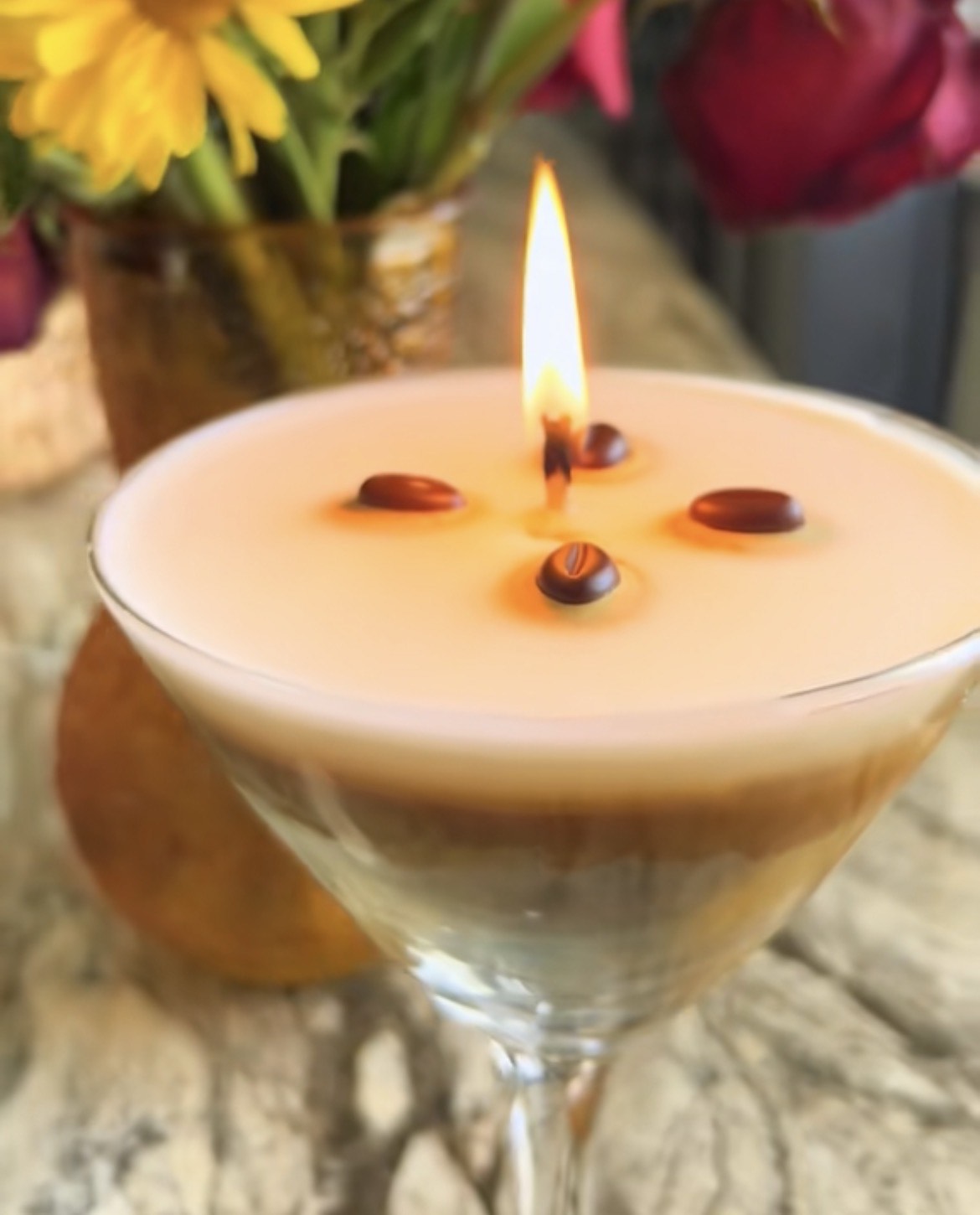 Close-up of a lit coffee martini candle  with flowers in the background.