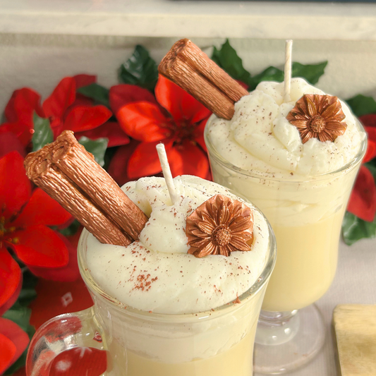 Top view of two Coquito Christmas candles showcasing whipped cream layers, cinnamon stick, and anise flower topping in Irish cups.