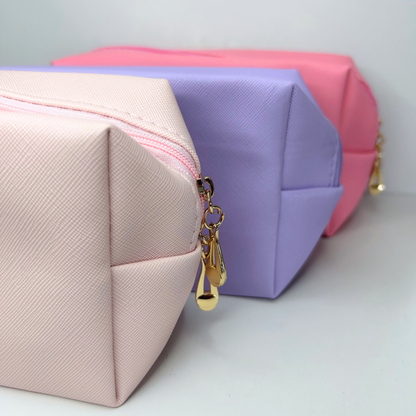 Trio of custom initial cosmetic pouches in purple, pink, and light pink – close-up view.