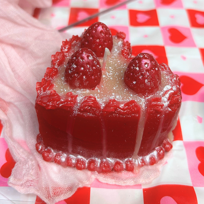 Red heart-shaped cake candle with strawberries on a checkered heart tablecloth.