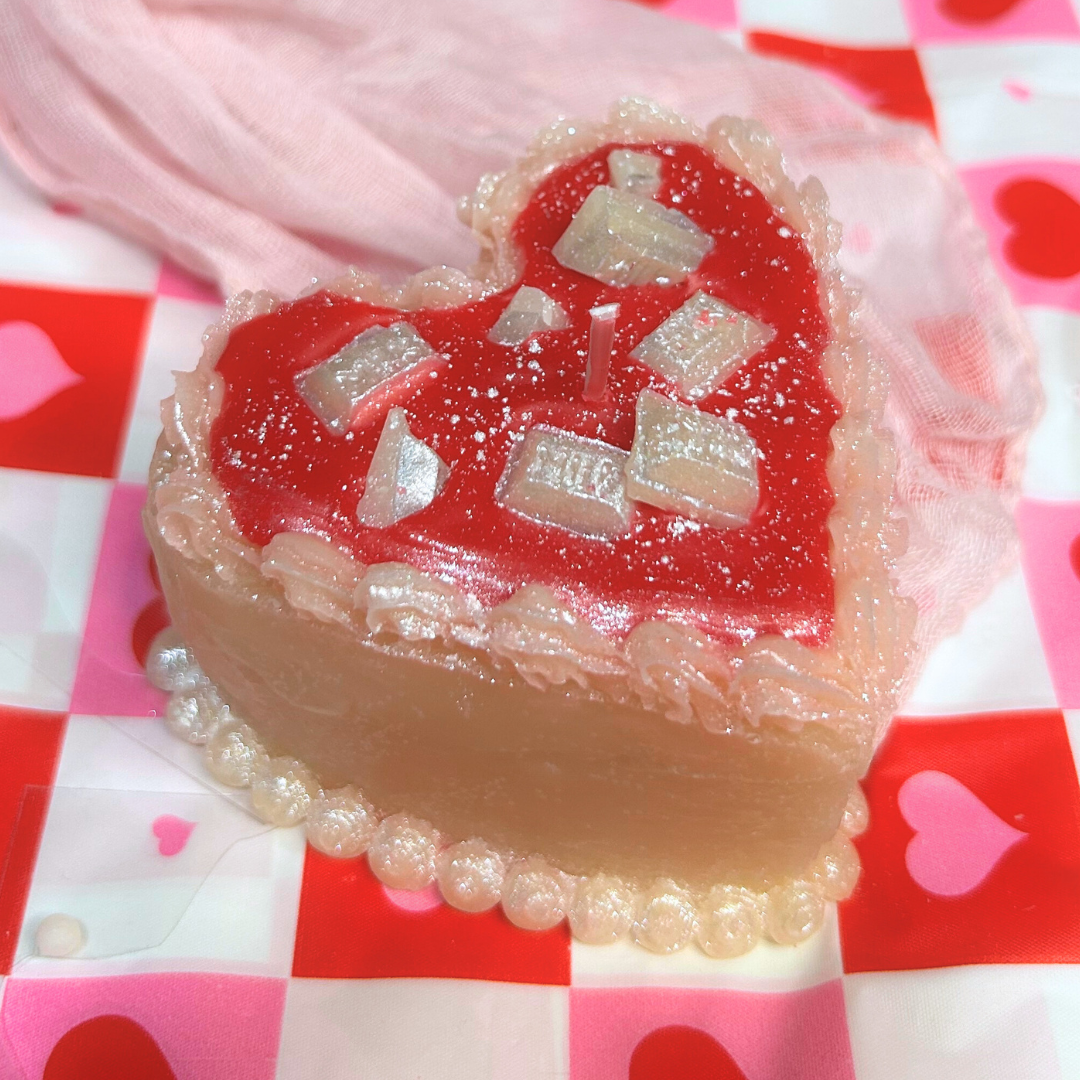 Heart-shaped dessert candle with red cream and white chocolate bars on a checkered background