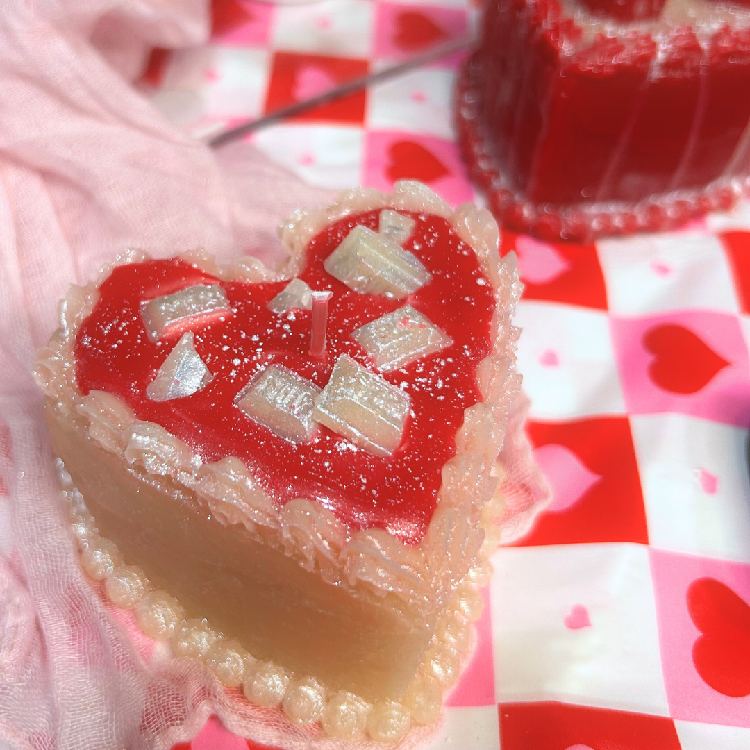 Heart-shaped dessert candle with red filling and white drizzle on a checkered heart tablecloth.
