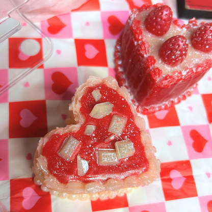 Heart-shaped red and white sweet dessert candles with strawberry and chocolate toppings on a checkered tablecloth with heart patterns.