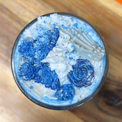 Top view of Emily’s Veil candle featuring white whipped wax, two blue roses, a blue butterfly, and a white bone hand.