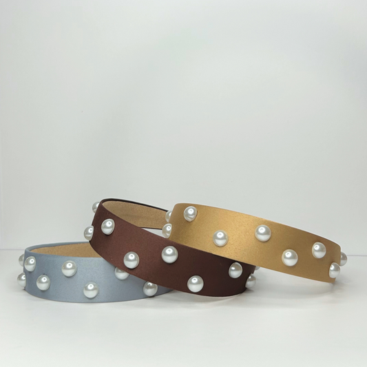 Front view of stacked pearl headbands in baby blue, brown, and gold, showcasing their elegant design and versatility.