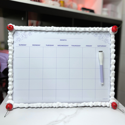 Dry erase calendar with decorative frosting and cherry frame and markers on a surface.