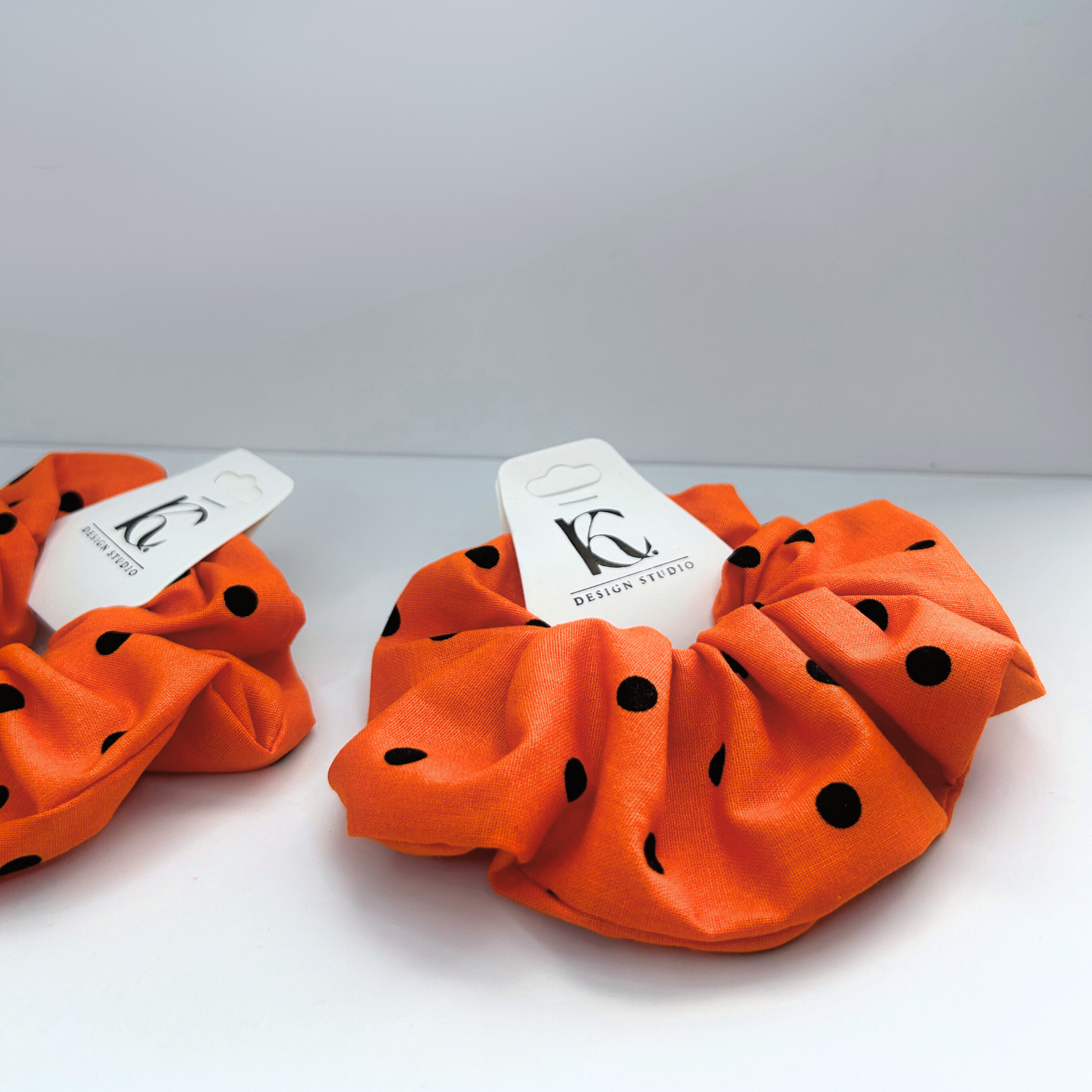 Closeup side view of orange Halloween scrunchie with black polka dots, featuring a 7-inch elastic for a secure fit.