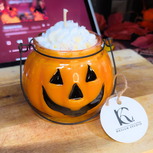 Halloween-themed candle in a jack-o'-lantern jar with a visible brand tag on a wooden surface.
