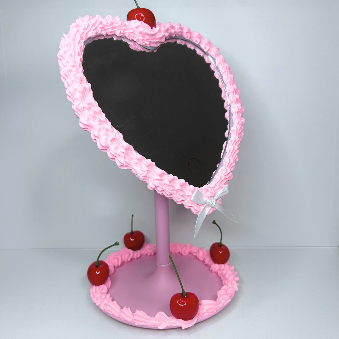 Bottom angled view of pink heart-shaped LED mirror showing pink frosting and cherry design.
