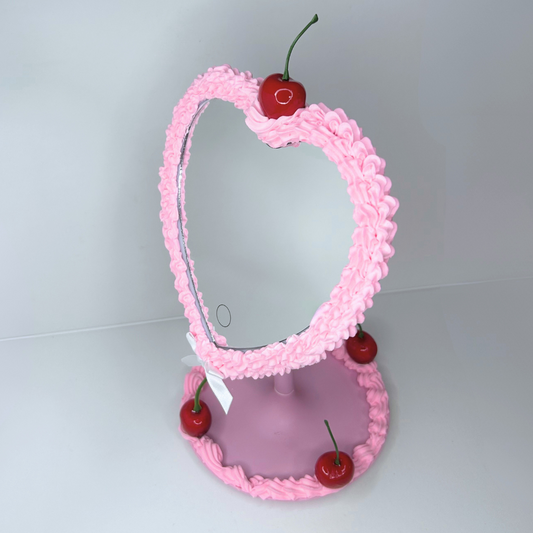 Front view of heart-shaped pink cake LED mirror with cherry frosting and glowing ring light.