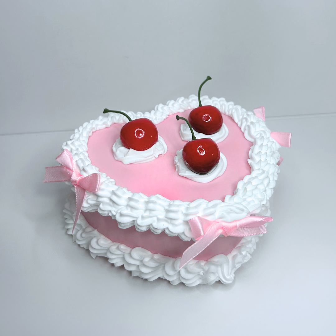 Front view of a vintage heart-shaped cake jewelry box with pink and white frosting design and red cherry decorations.