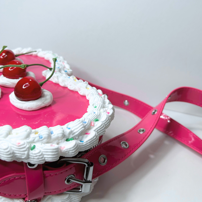 Pink cake-shaped handbag with whipped cream and cherries on a white background