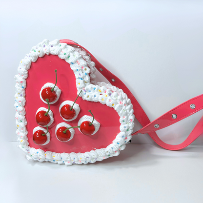 Pink heart-shaped cake with red cherries and white frosting on a white background