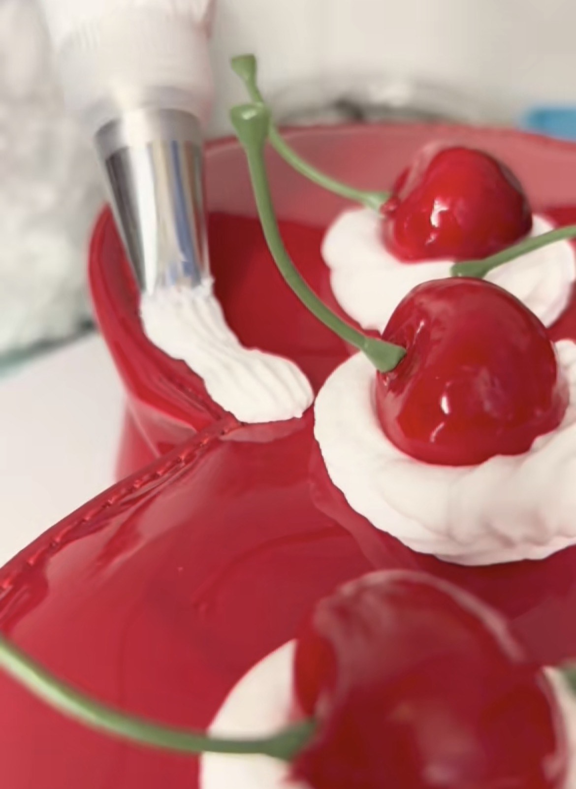 Close-up image of a red heart-shaped purse being decorated with white frosting and cherries.