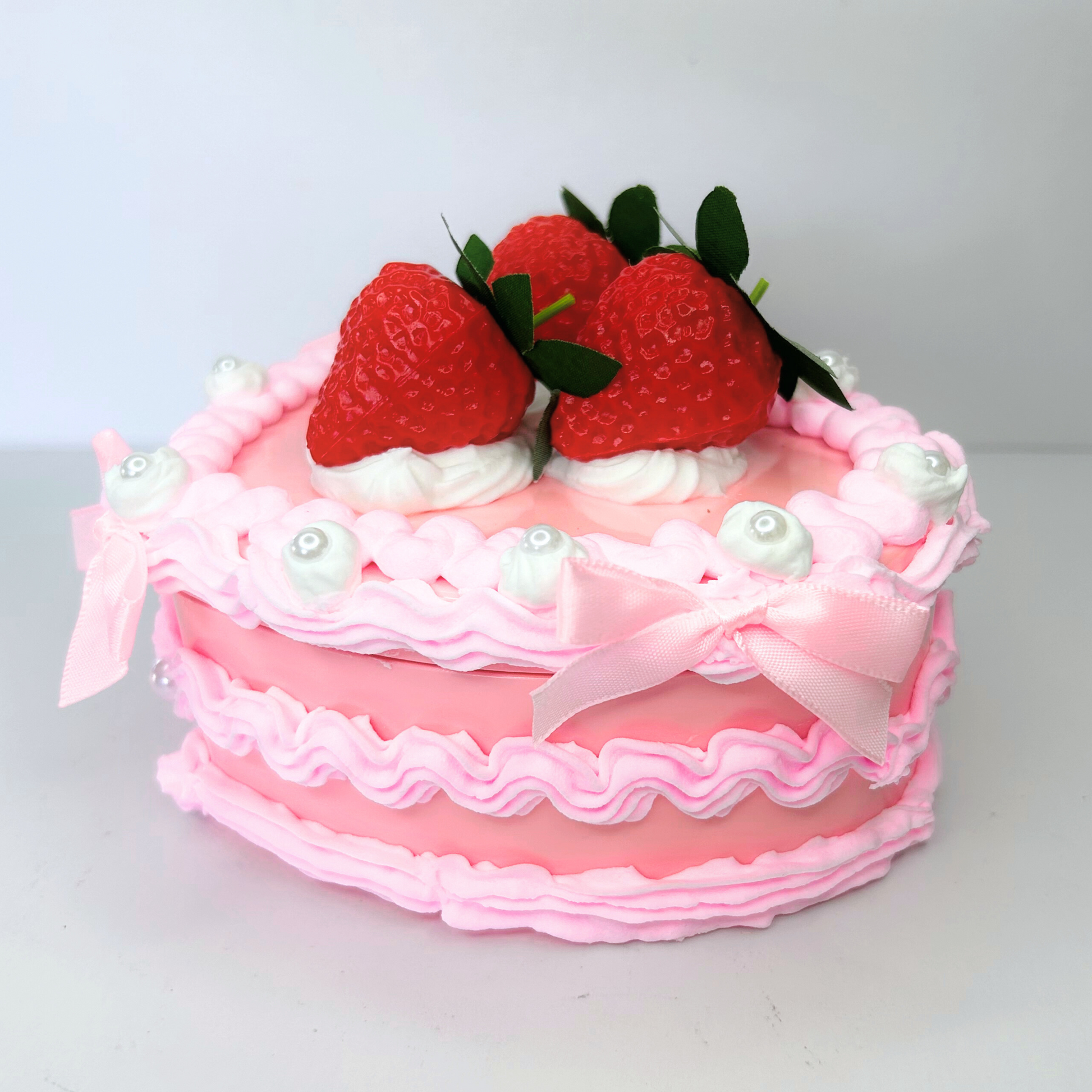 Side view of a heart-shaped vintage jewelry box featuring a pink and white design, adorned with three strawberries, pearls, and mini pink bows.