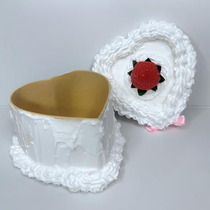 Open heart-shaped cake-inspired storage box with pink bow and centered strawberry.