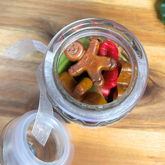 Top view of Jolly Melts wax melts inside a glass candy jar, showing red and green candy canes and gingerbread men.