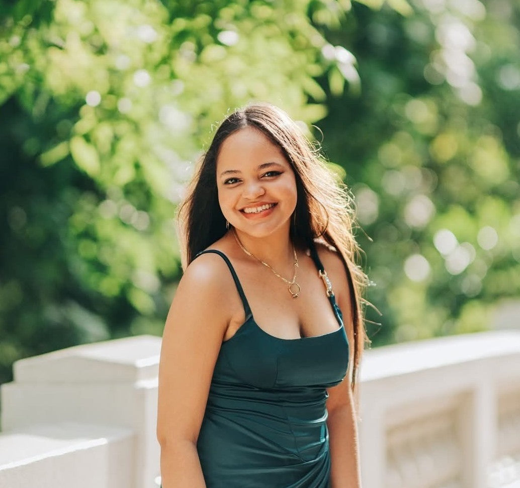 Woman in a green dress standing outdoors with trees in the background.