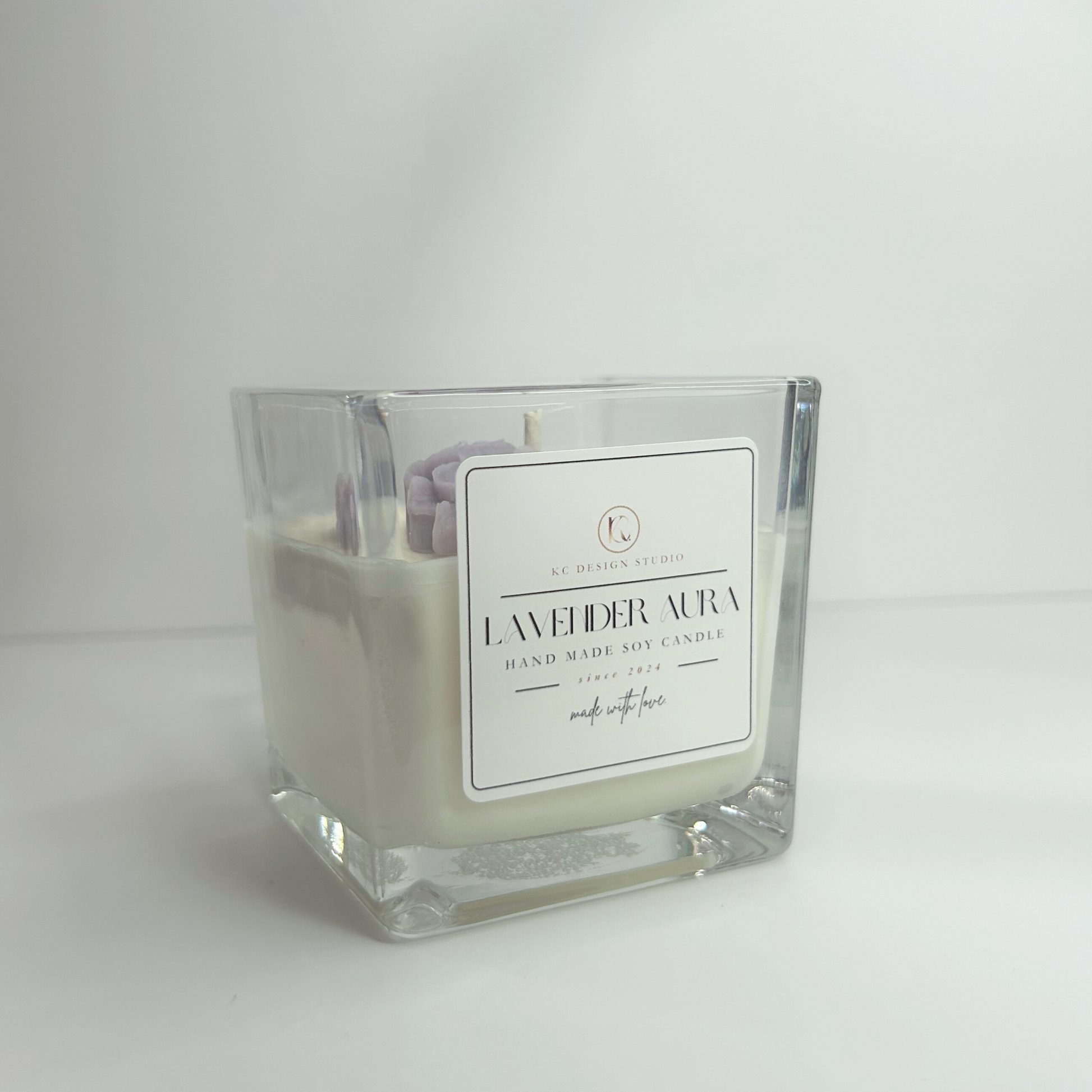 Side view of the 10oz Lavender Aura Candle, showcasing its square shape and elegant design topped with soft purple wax flowers.