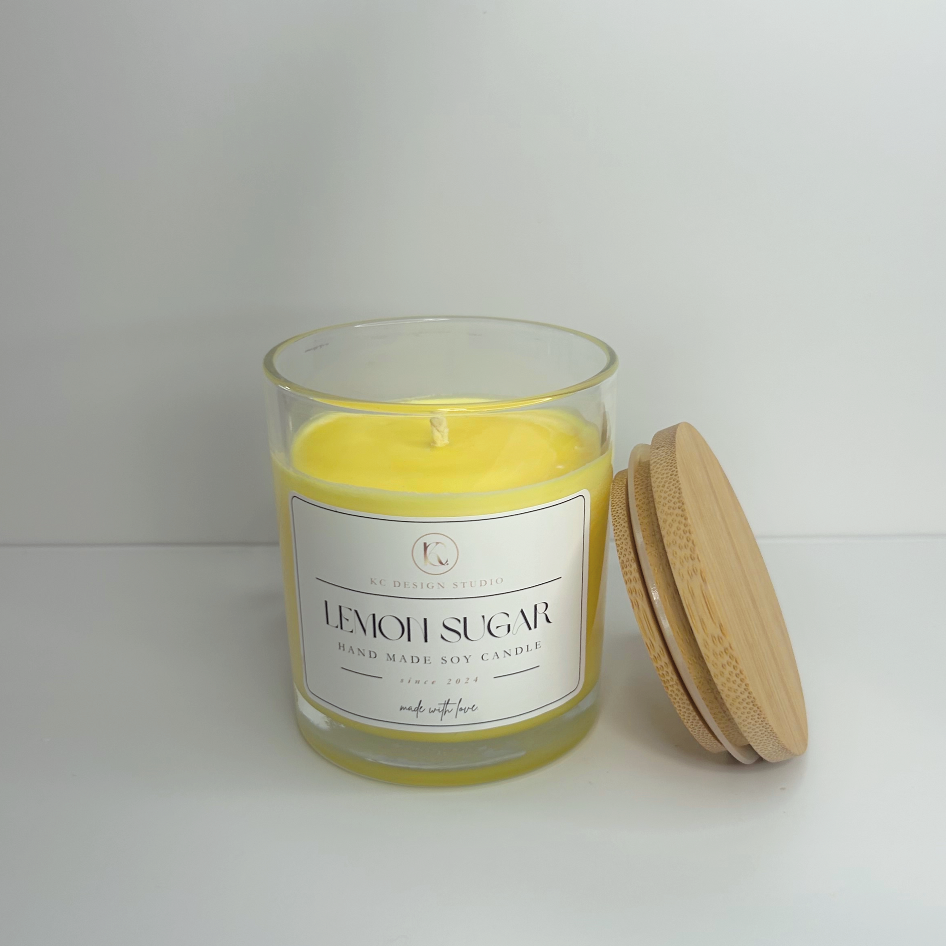 Top view of the 10oz Lemon Sugar Candle with lid resting on side, featuring its smooth surface and bright yellow color, inviting you to enjoy its refreshing aroma.